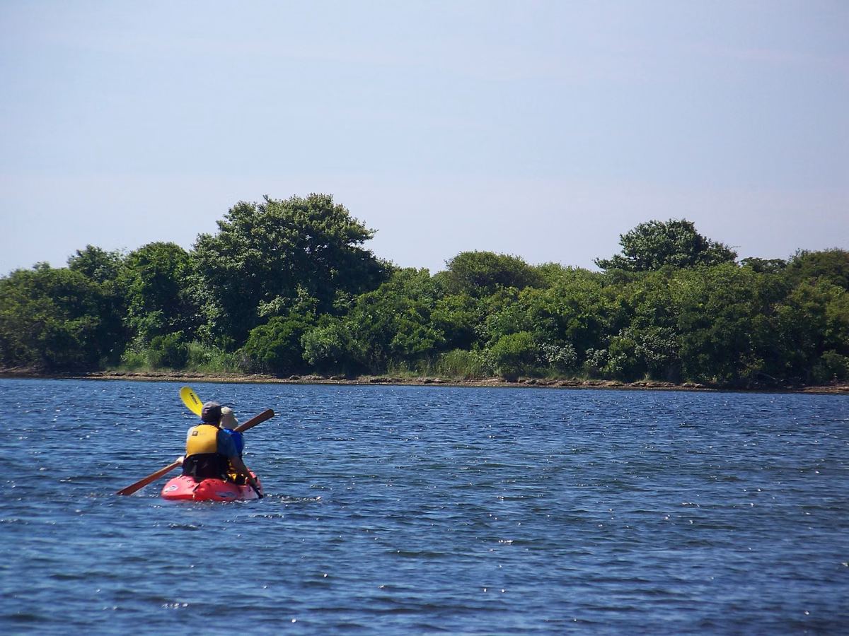 A kayaker paddling a red kayak on a salt pond in Charlestown